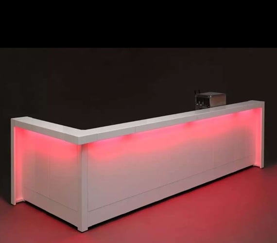 White reception desk with pink-red LED underlighting along the base, set in a dark room for a modern look.