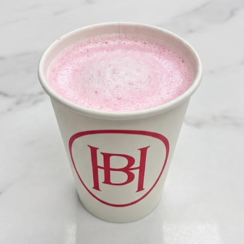 White paper cup with pink frothy drink on a marble surface, featuring a red HBH logo on the front.