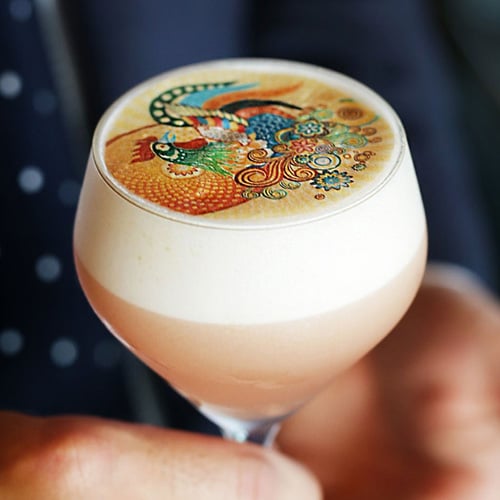 Tulip-glass beer with a thick foamy head topped by a colorful ornate design on the surface.