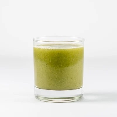 Green smoothie in a short glass on a white surface with a frothy top.